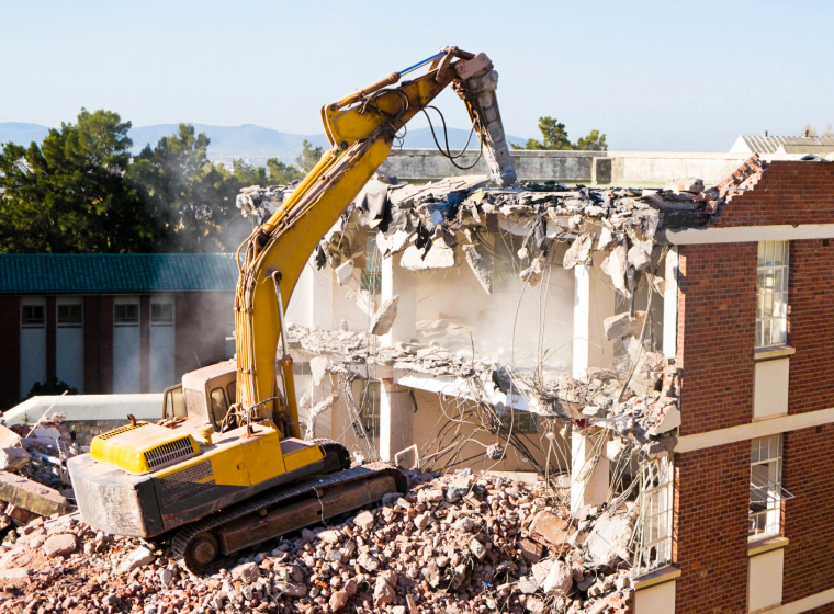 yellow demolition machine on top of debris demolishing a building